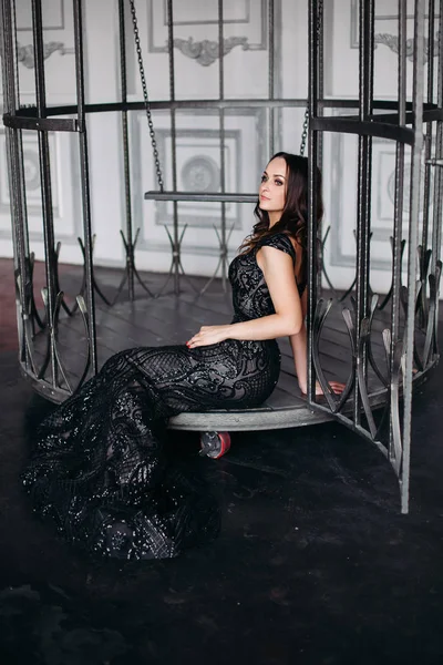 Hermosa mujer morena con vestido negro brillante posando en jaula como pájaro . —  Fotos de Stock