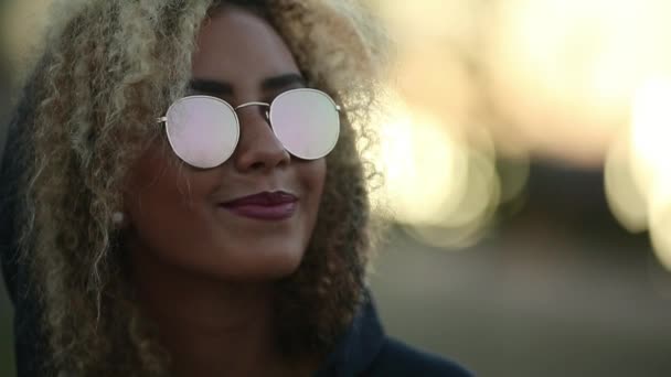 Hipster girl avec des cheveux blonds bouclés et des lunettes de soleil en miroir regardant loin et souriant . — Video
