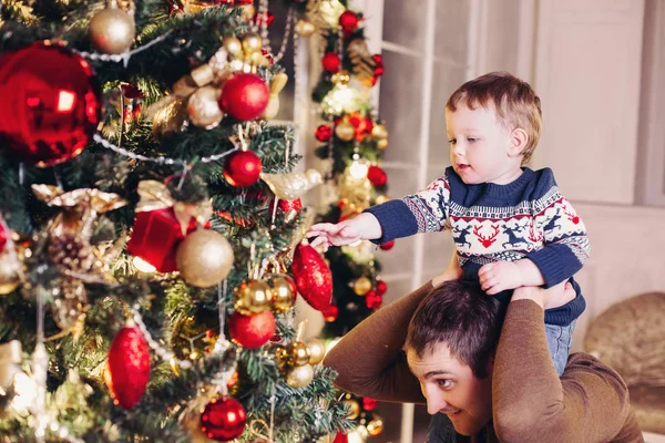 小さな息子のための木の上にクリスマスの装飾を示す幸せな両親. — ストック写真