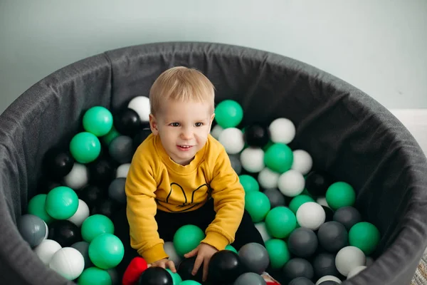 Kleiner Junge sitzt mit bunten Plastikbällen im Bällebad und lächelt. — Stockfoto