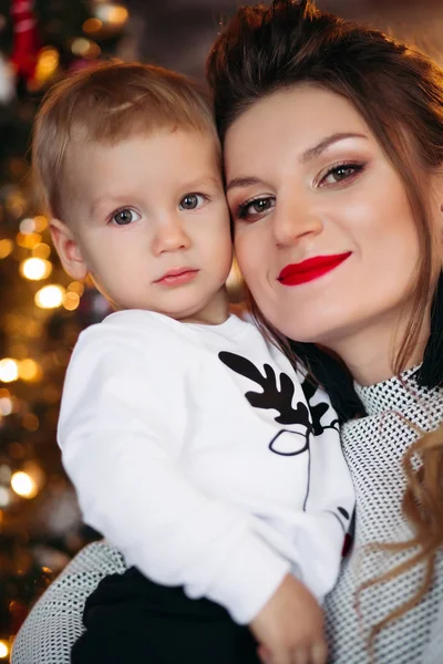 Liefdevolle mooie moeder met baby tegen kerstboom. — Stockfoto