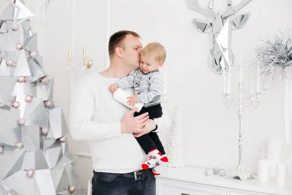 Padre encantador manteniendo hijo en las manos, abrazándolo y besándolo en el estudio de Navidad —  Fotos de Stock