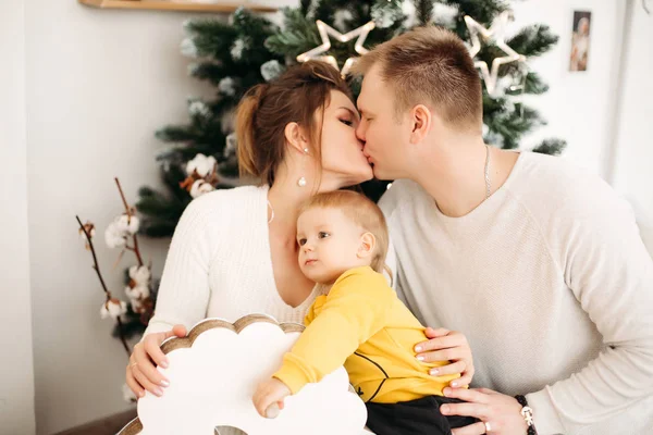 Pais felizes no amor abraçando e beijando sentado no fundo perto da árvore de Natal . — Fotografia de Stock