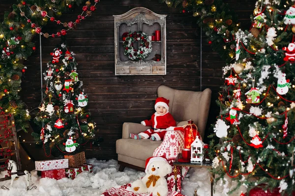 Piccolo Babbo Natale in suite rossa seduto su una grande poltrona vicino all'albero di Natale . — Foto Stock