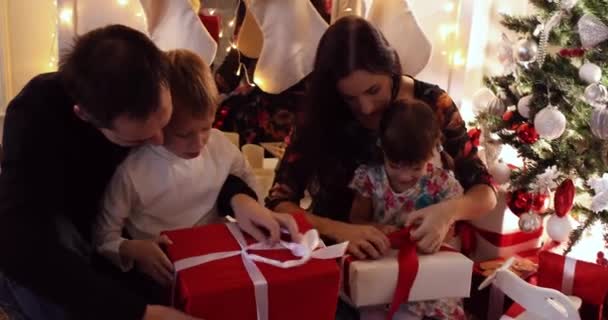 Alegre padres presentando regalos de Navidad a sus hijos por árbol decorado . — Vídeo de stock