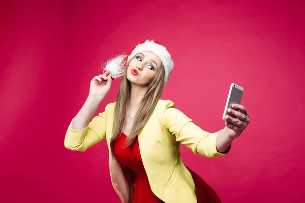 惊讶的女人在圣诞老人帽子使自拍在粉红色的背景. — 图库照片