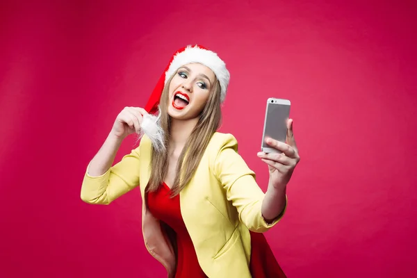 惊讶的女人在圣诞老人帽子使自拍在粉红色的背景. — 图库照片