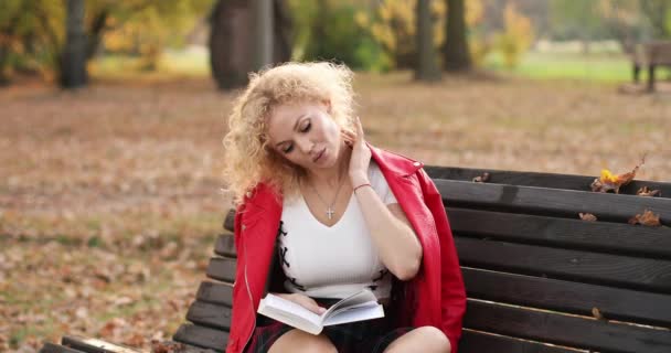 Chica sentada en un piso de madera, leyendo un libro, al aire libre . — Vídeos de Stock