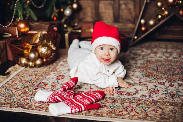 Bayi manis yang bahagia dengan topi merah di karpet dengan sarung tangan musim dingin yang lucu . — Stok Foto