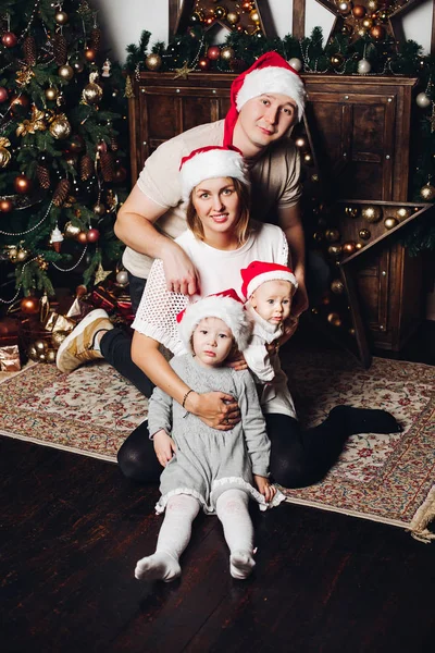 Gelukkige familie in rode Santa hoeden bij de kerstboom. — Stockfoto