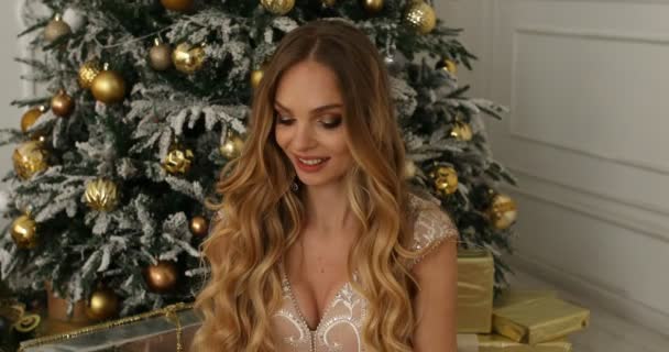 礼品盒和微笑的女人在圣诞树背景。美丽的金发与长光的头发开放的礼物和微笑 — 图库视频影像