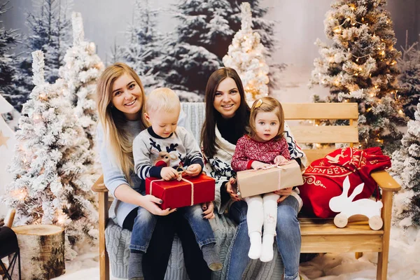 Két anya ül a aranyos gyerekek, és a gazdaság karácsony bemutat. — Stock Fotó