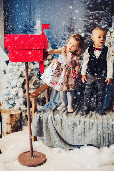 Двоє маленьких дітей грають із зеленими різдвяними бантами біля прикрас та ялинки . — стокове фото