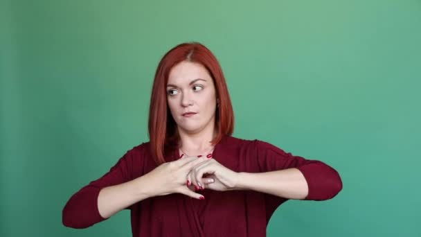 Red haired woman posing at studio on green background, pulls out ring from finger. — Stock Video