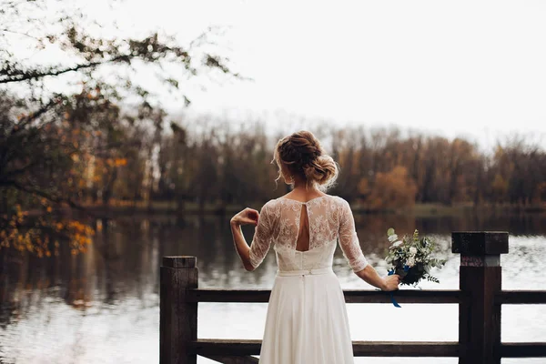 Elegante sposa in abito da sposa bianco con bouquet sul lago . — Foto Stock