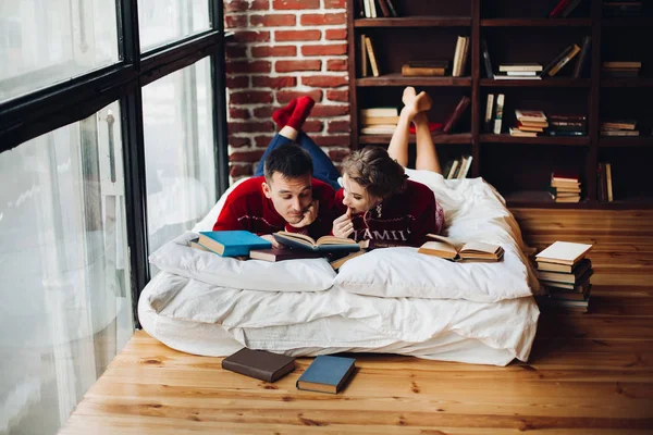 Paar im roten Weihnachtspulli liest Bücher auf Matratze bei hom — Stockfoto