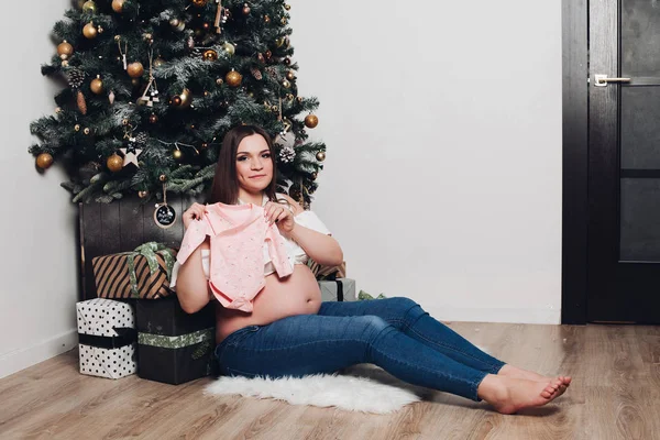 Mujer embarazada posando con traje de bebé. Mujer feliz sosteniendo lindo traje de bebé . — Foto de Stock