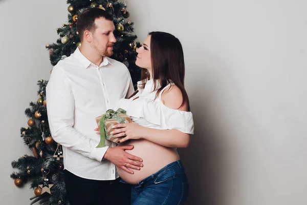 Man en zwangere vrouw poseren in de buurt van de kerstboom. — Stockfoto