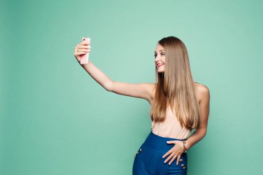 Güzel bir kadın yeşil arka planda cep telefonuyla selfie çekiyor..