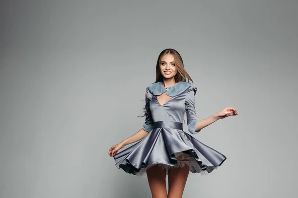 Retrato de estúdio de uma menina loira com cabelos longos em um vestido curto e exuberante. O vestido levantou-se do vento e do movimento da menina. Isolado em um fundo cinza . — Fotografia de Stock