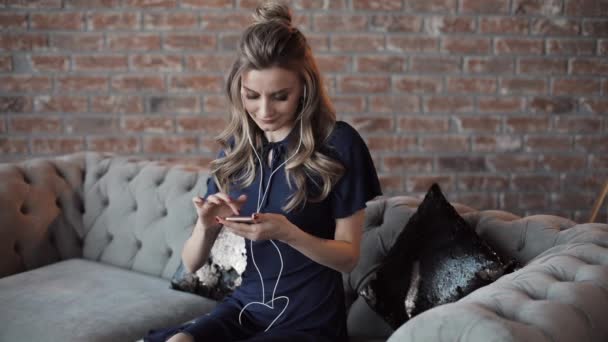 Optimistisch blonde vrouw in jurk luisteren naar de muziek op haar mobiel. — Stockvideo