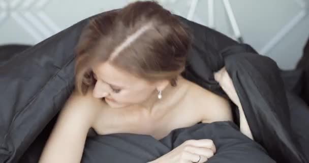 Jolie jeune femme regardant sous la couverture, souriant à la caméra . — Video