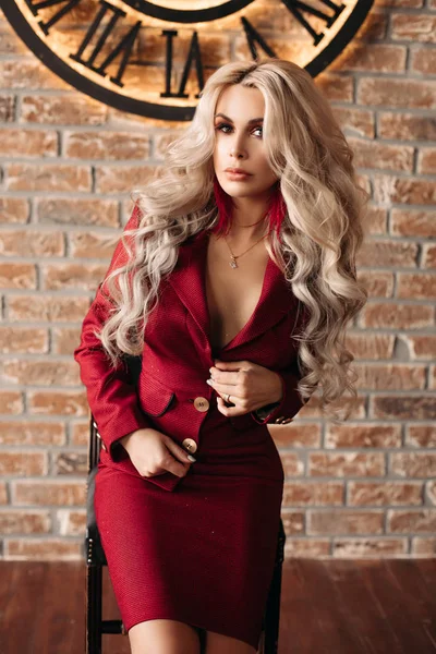 Mujer rubia seductora en traje rojo posando contra reloj . — Foto de Stock