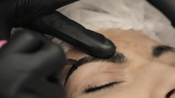 Close-up, de handen van de schoonheidsspecialist in zwarte rubber toepassing van permanente make-up op wenkbrauwen-wenkbrauw tattoo — Stockvideo
