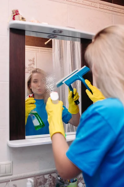 Limpieza de la mujer con spray y el uso de la escobilla para lavar el espejo en el baño . — Foto de Stock