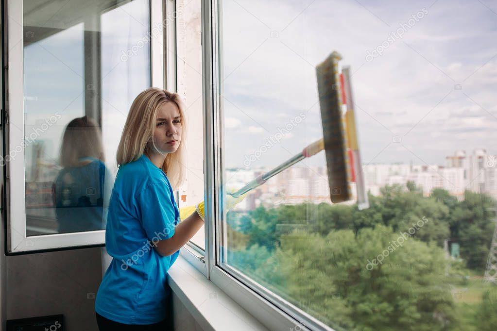 Young girl wearing in rubber gloves with special brush cleaning large open window.