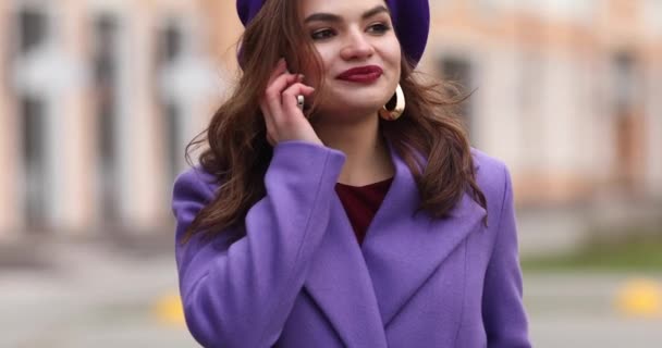 Elegantní žena v purpurovém plášti a baret mluvit na telefonu v ulici. — Stock video