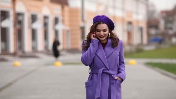 Elegantní žena v purpurovém plášti a baret mluvit na telefonu v ulici. — Stock video