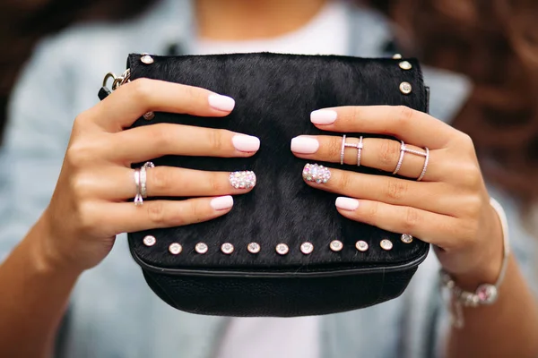Meisje met gemanicuurde nagels met een mooi sieraad in trouwringen die zwarte vacht tas. — Stockfoto