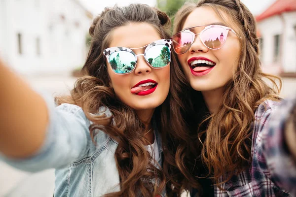 Hermosas amigas morenas con peinado, gafas de sol espejadas y labios rojos haciendo selfie con cara de pato . — Foto de Stock