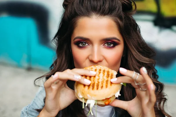 Chica con maquillaje brillante tomando un bocado de hamburguesa. — Foto de Stock