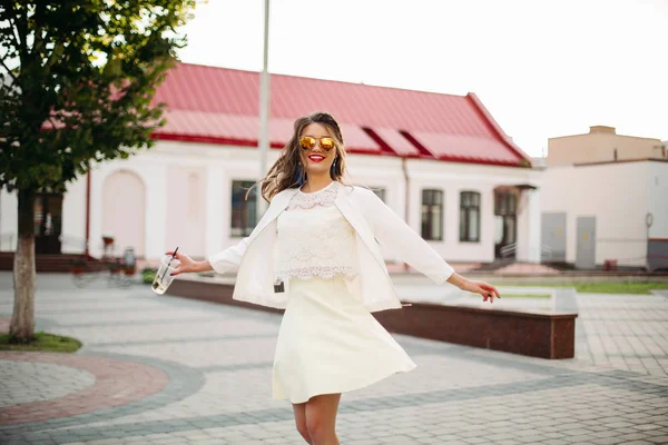 Счастливая девушка в солнечных очках в белом свете танцует на улице . — стоковое фото