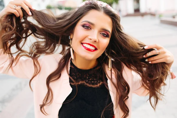 Beautiful brunette girl with bright make up holding her hair and smiling at camera. — Stock Photo, Image