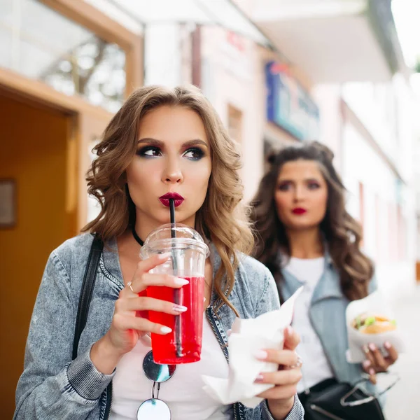 패스트 푸드 및 음료와 함께 거리에 걷는 두 세련 된 장식 여자. — 스톡 사진