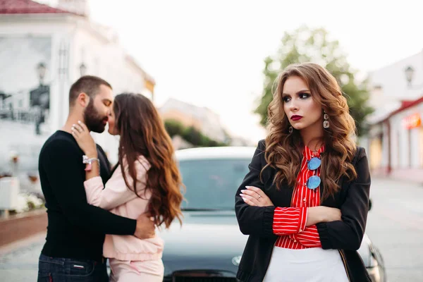 Çift öpüşme karşı moda giysiler katlanmış kollarında hüzünlü güzel bir kadınla.