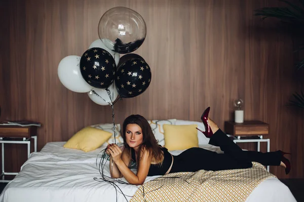 魅力的なモデルがベッドに横になっていると、黒と白の風船を保持. — ストック写真