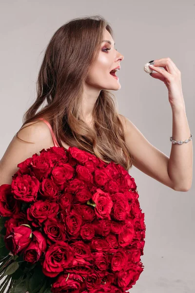 Morena senhora com um monte de rosas vermelhas comendo doce . — Fotografia de Stock