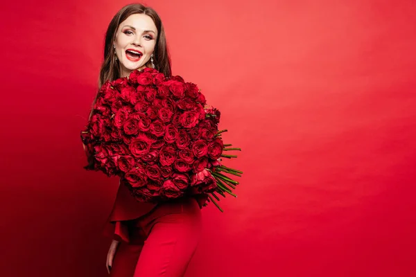 장미 꽃다발을 유지 하는 빨간 드레스에 화려한 여자 — 스톡 사진