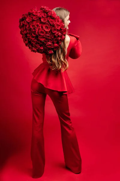 Jovem morena feliz em vestido vermelho segurando grande monte de rosas vermelhas . — Fotografia de Stock