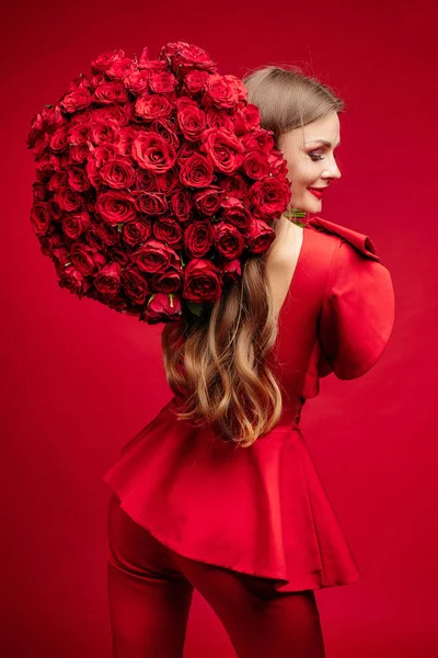 Eerlijke haired elegante vrouw in rode kleding houden van bloemen. — Stockfoto