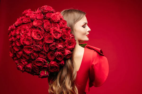 Bella giovane signora bruna in rosso con mazzo di rose rosse sulla spalla . — Foto Stock