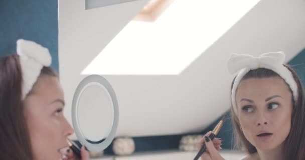 Linda senhora olhando para o espelho e fazendo maquiagem em casa — Vídeo de Stock