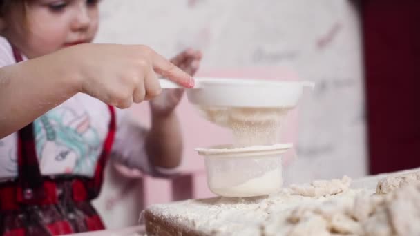 Schattig meisje zeven bloem door zeef op keuken — Stockvideo