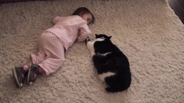 Küçük kız yerde oturan ve kırmızı kabarık kedi ile oynuyor.