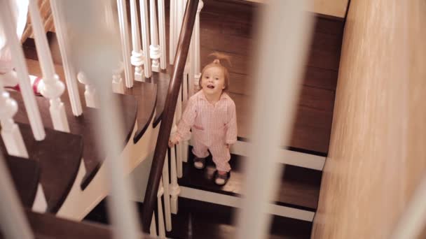 Small girl in pink pyjama sitting on stairs and playing — Stock Video