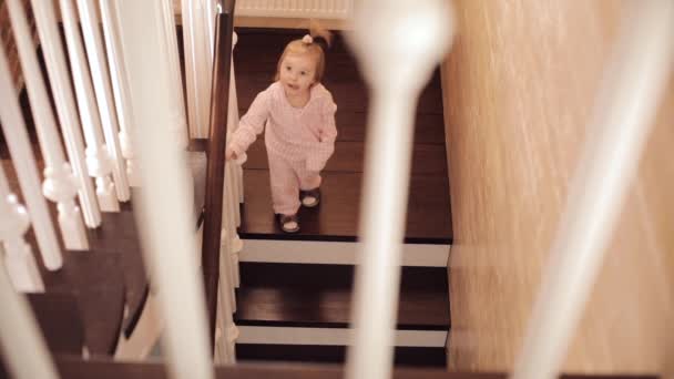 Маленька дівчинка в рожевій піжамі сидить на сходах і грає — стокове відео